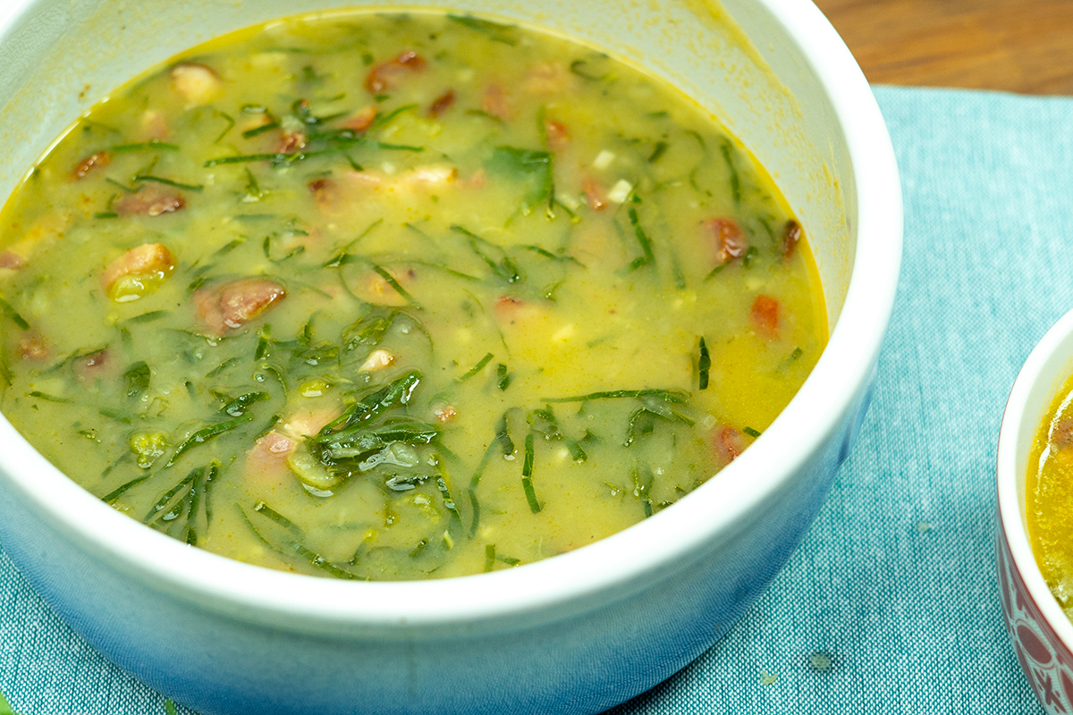 Creamy Caldo Verde served in a bowl with kale ribbons and slices of Portuguese sausage.