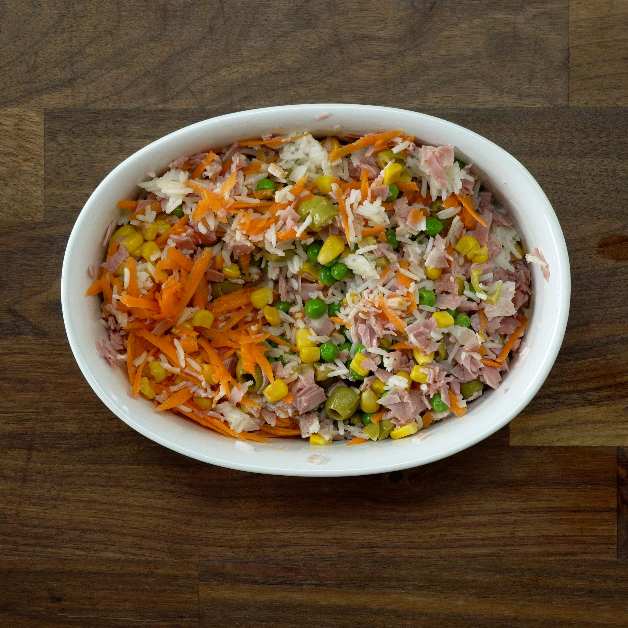 Cooked rice mixed with vegetables, bacon, and ham in a baking dish.