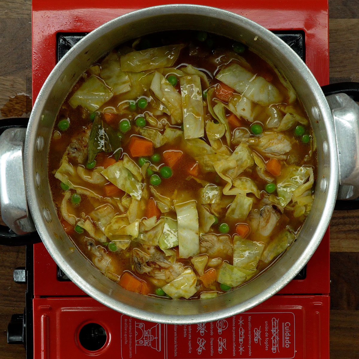 Pressure cooker with chicken, rice, vegetables, cabbage, bay leaf, and hot water before sealing.