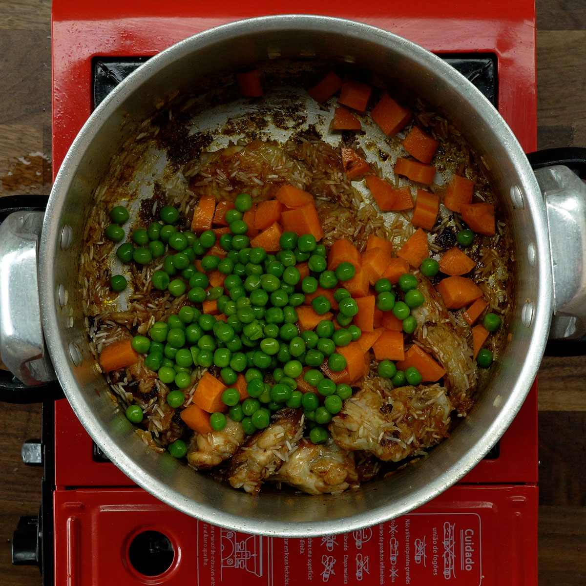 Rice and vegetables being added to the pot with chicken.
