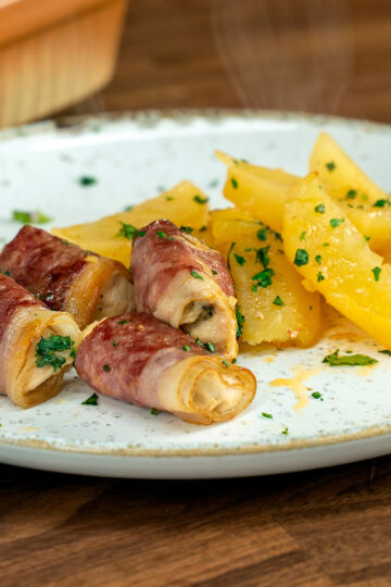 Plated bacon wrapped chicken bites with potatoes and parsley garnish.