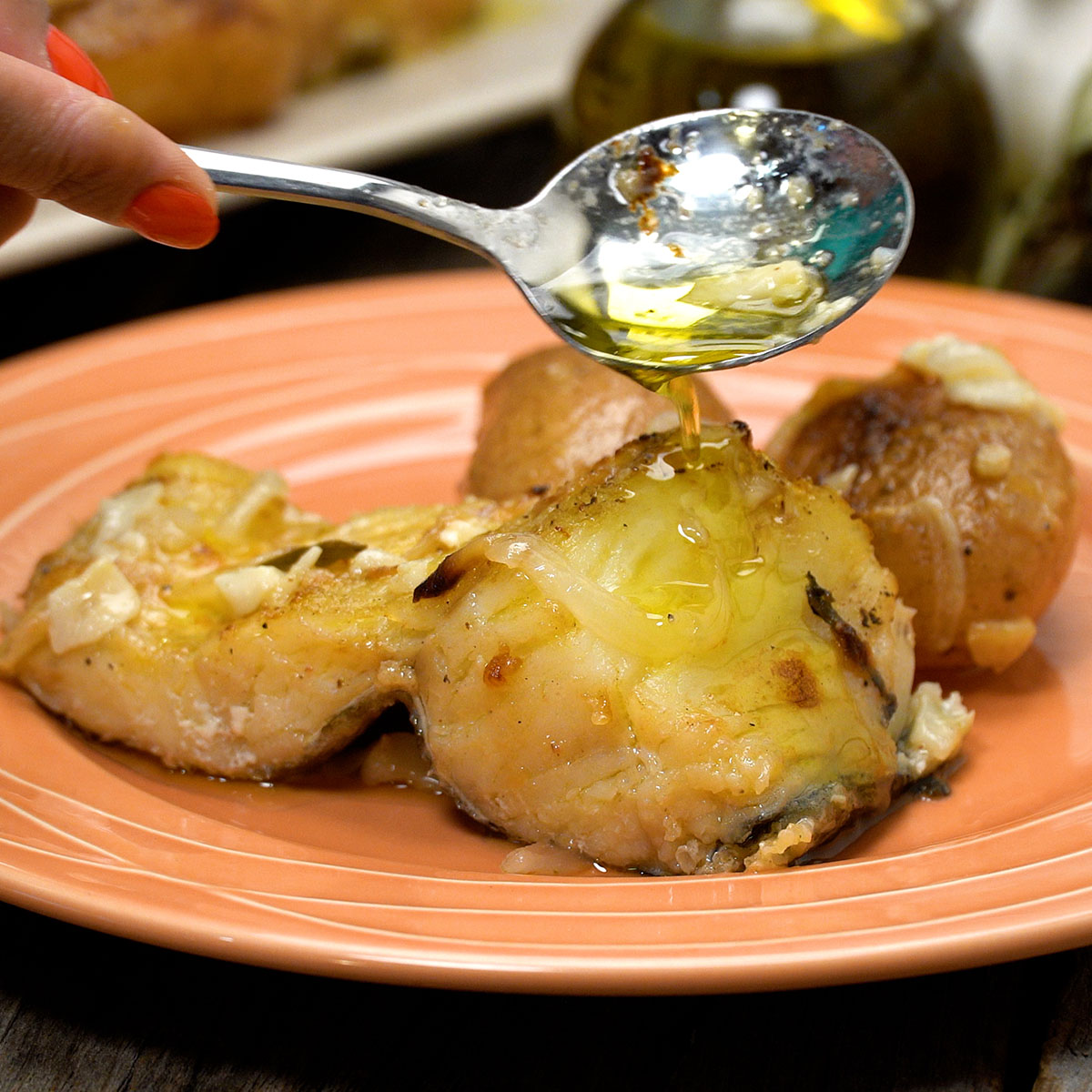 Baked cod on a plate being drizzled with hot olive oil and garlic