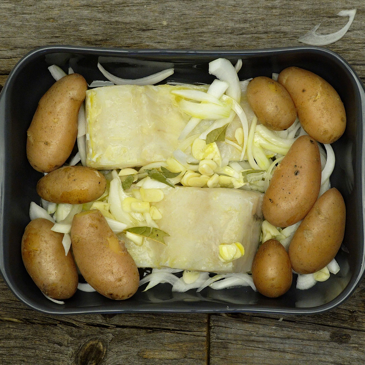 Small potatoes added to a baking dish with cod, onion and garlic