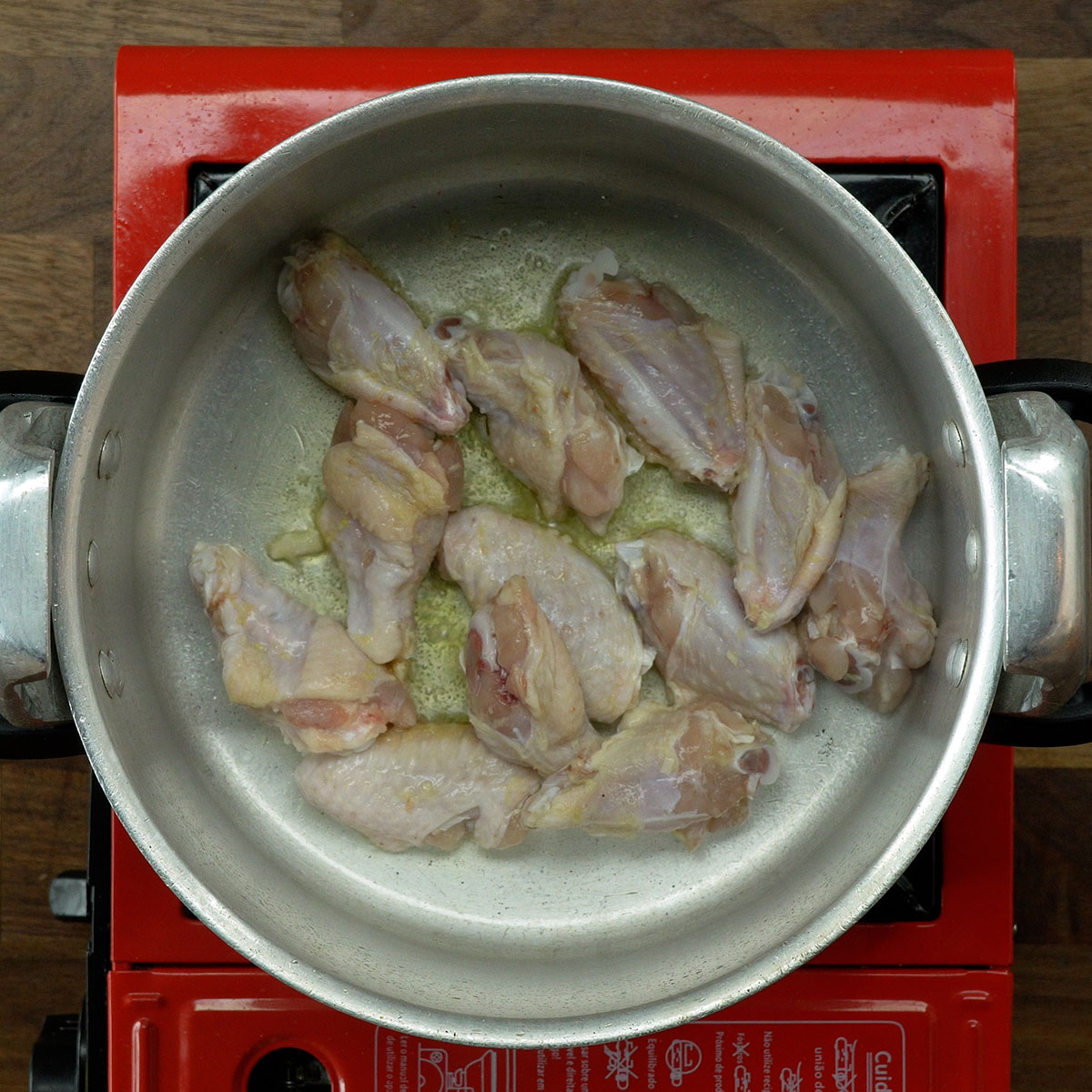 Chicken wings browning in a pressure cooker with olive oil.