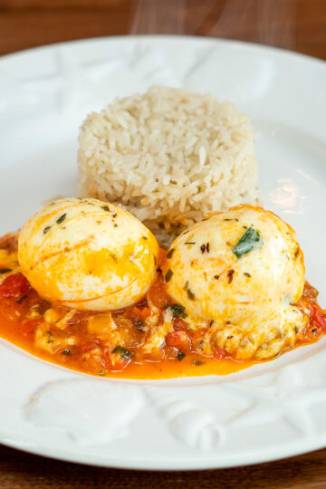 Plate of cheesy eggs in tomato sauce served with white rice.