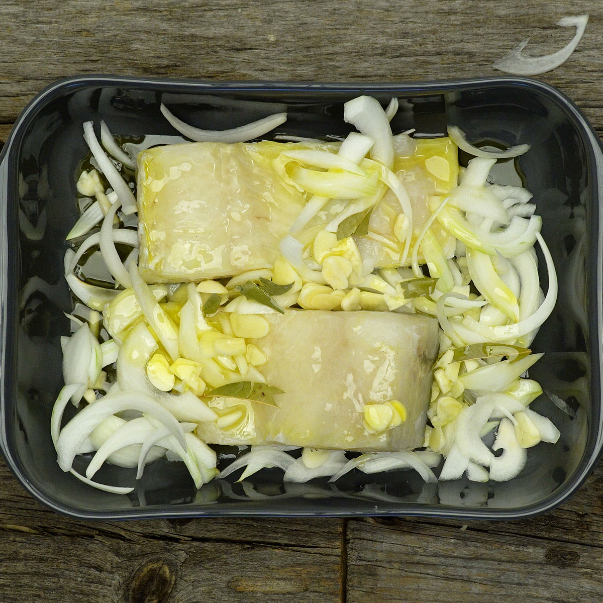 Cod in a baking dish with garlic, onion, bay leaves and olive oil