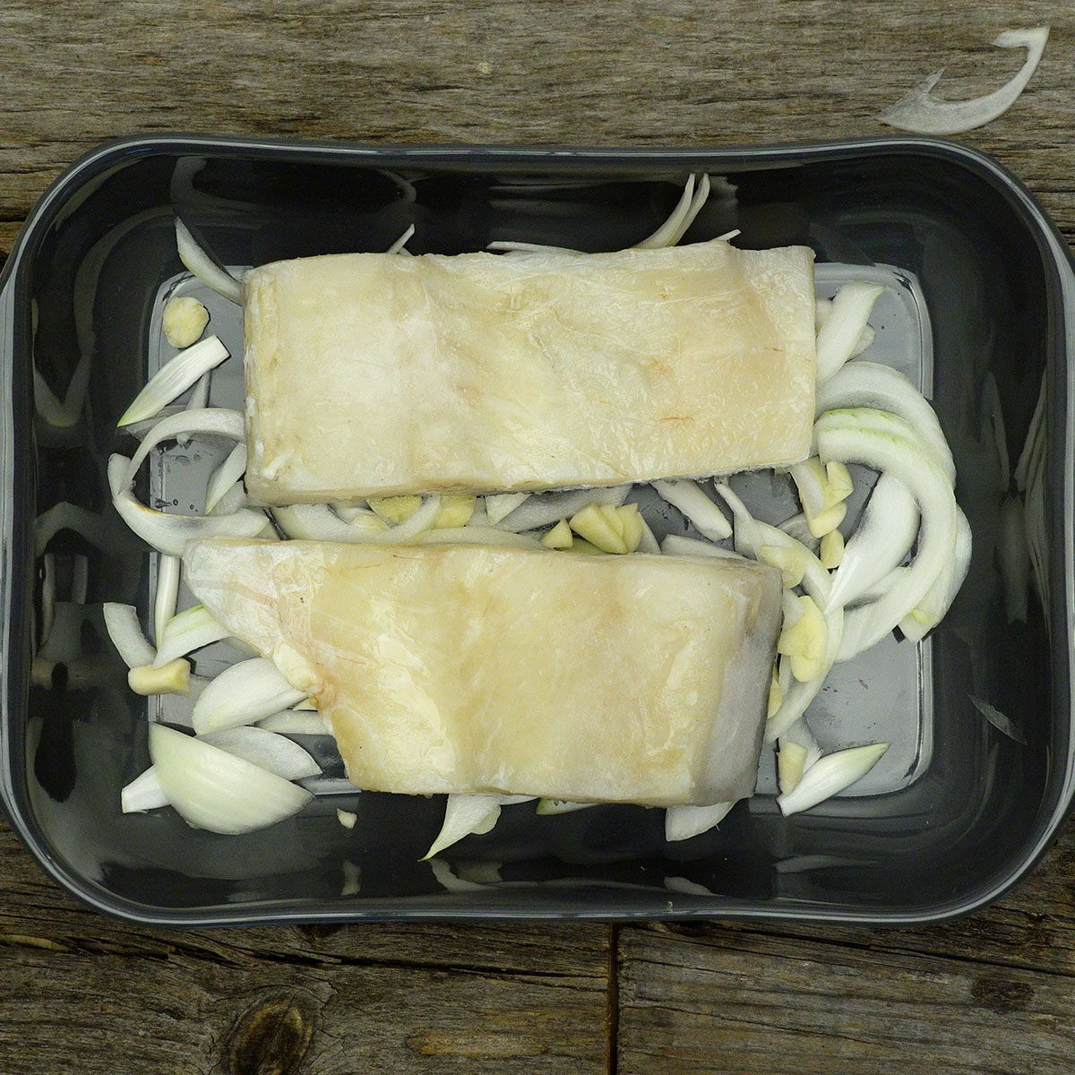 Raw cod loins placed over onions and garlic in a baking dish