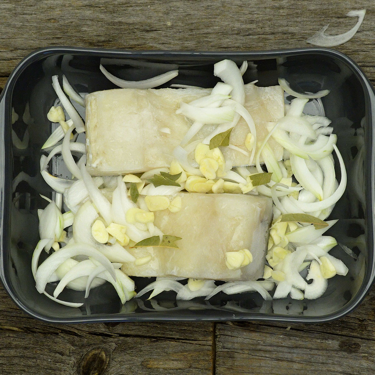 Cod pieces topped with sliced garlic, onion and bay leaves