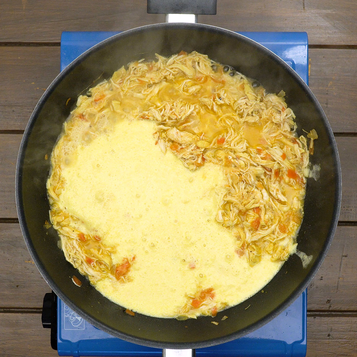 Creamy corn sauce with chicken being stirred in a pan.