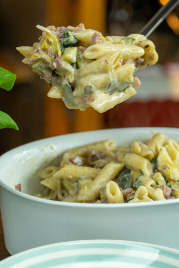 Creamy penne with bacon and zucchini being served.