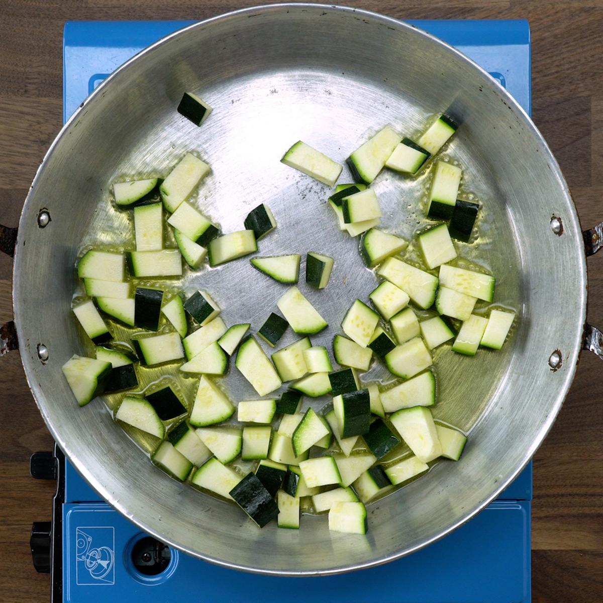 Diced zucchini being sautéed in a skillet.