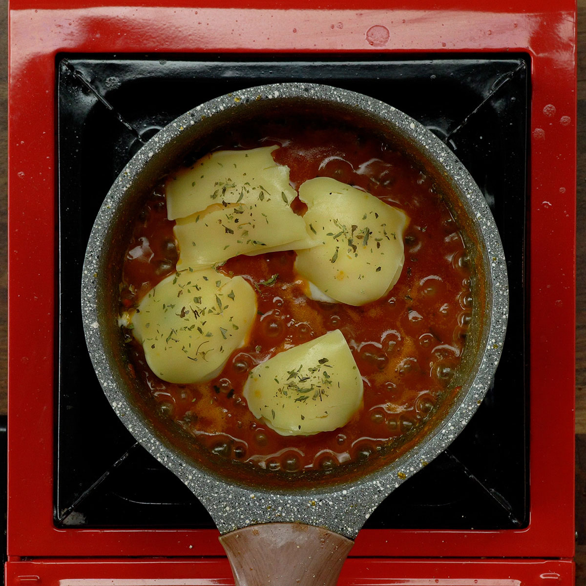 Eggs covered with mozzarella cheese and oregano in a skillet.