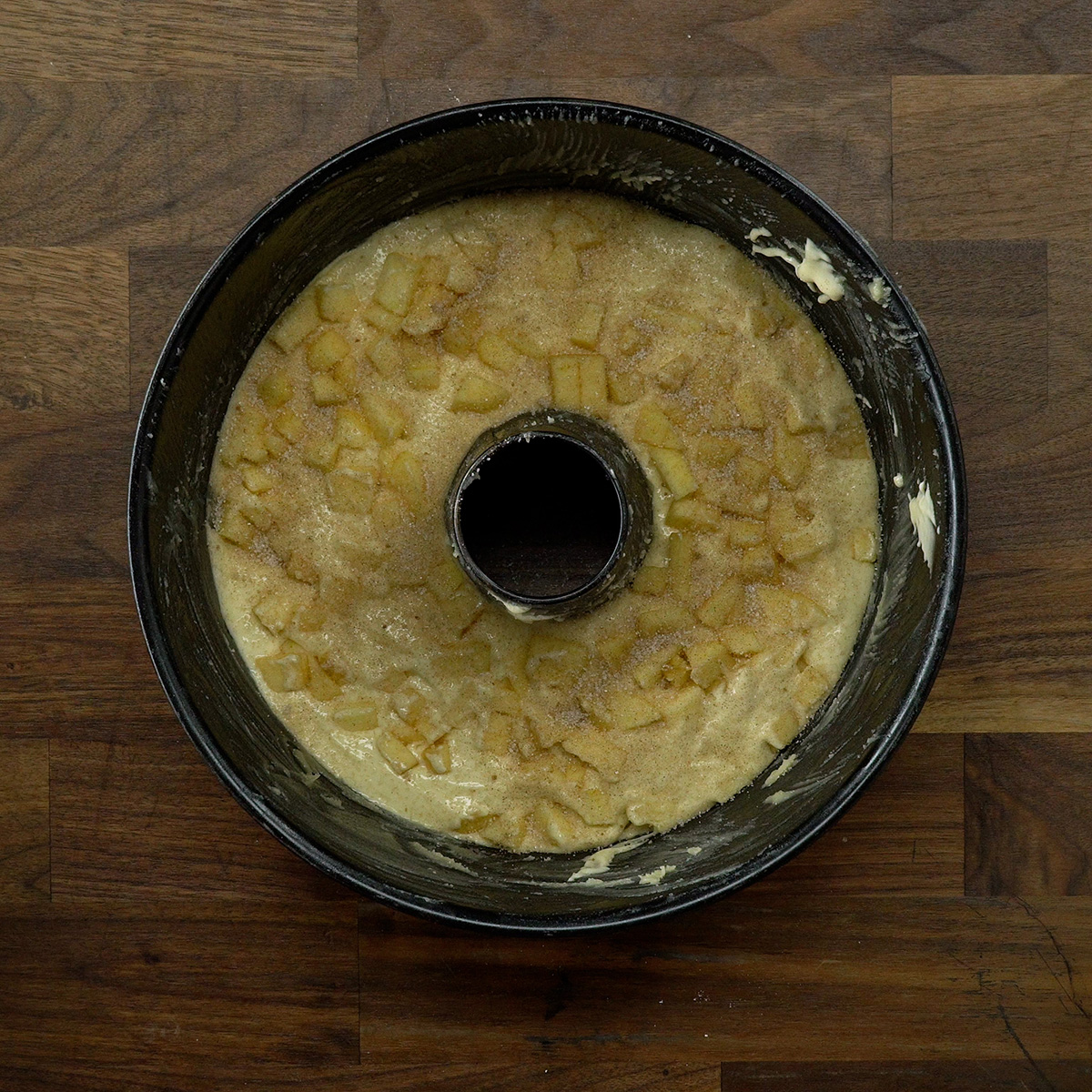 Apple cinnamon cake being layered with diced apples and cinnamon sugar.