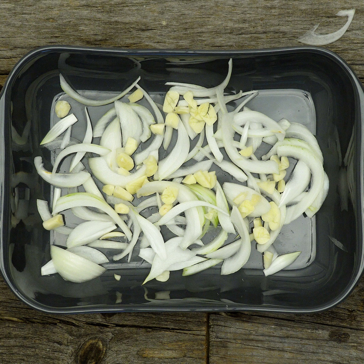 Sliced onion and garlic arranged in a baking dish for cod