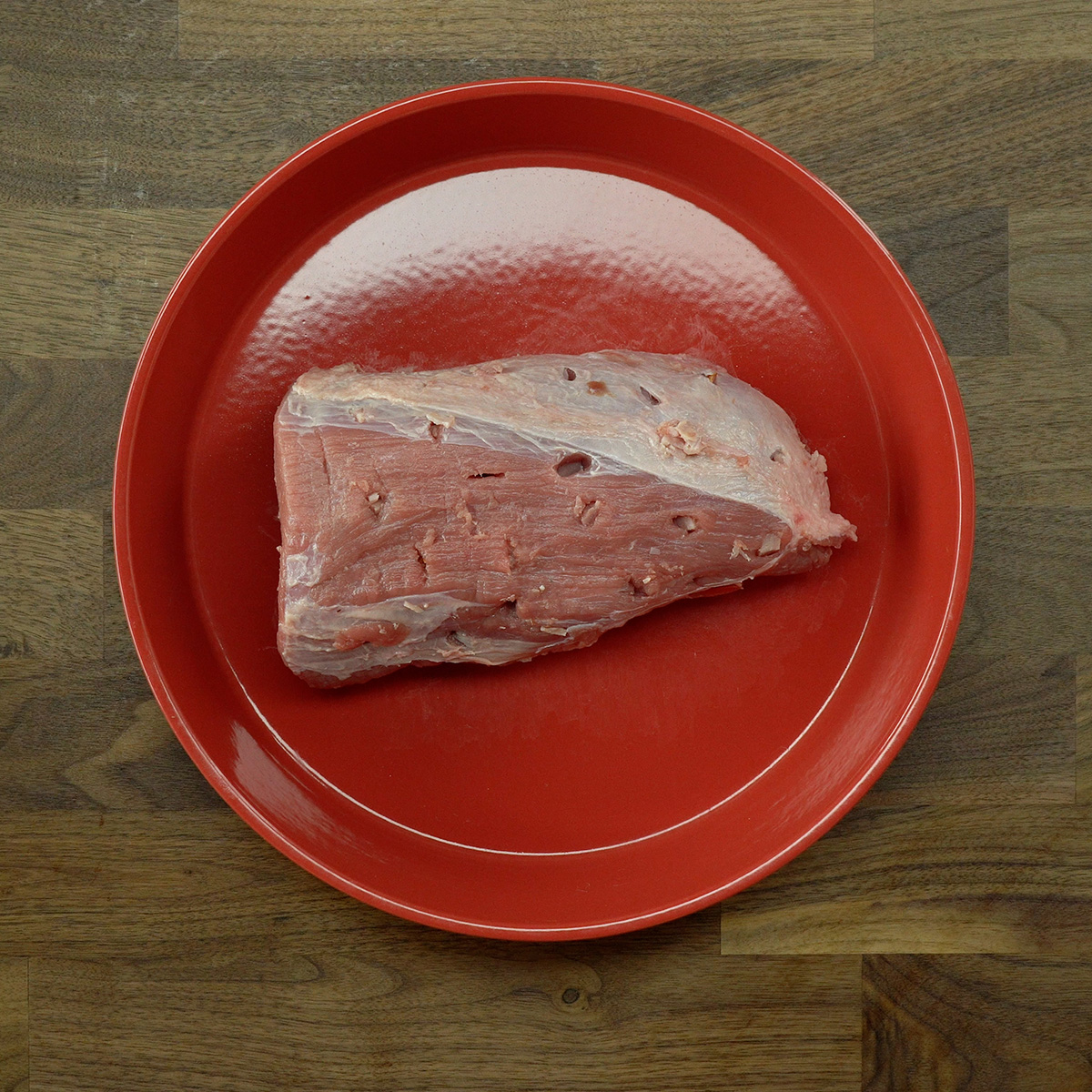 Raw eye of round roast with small cuts stuffed with diced bacon.