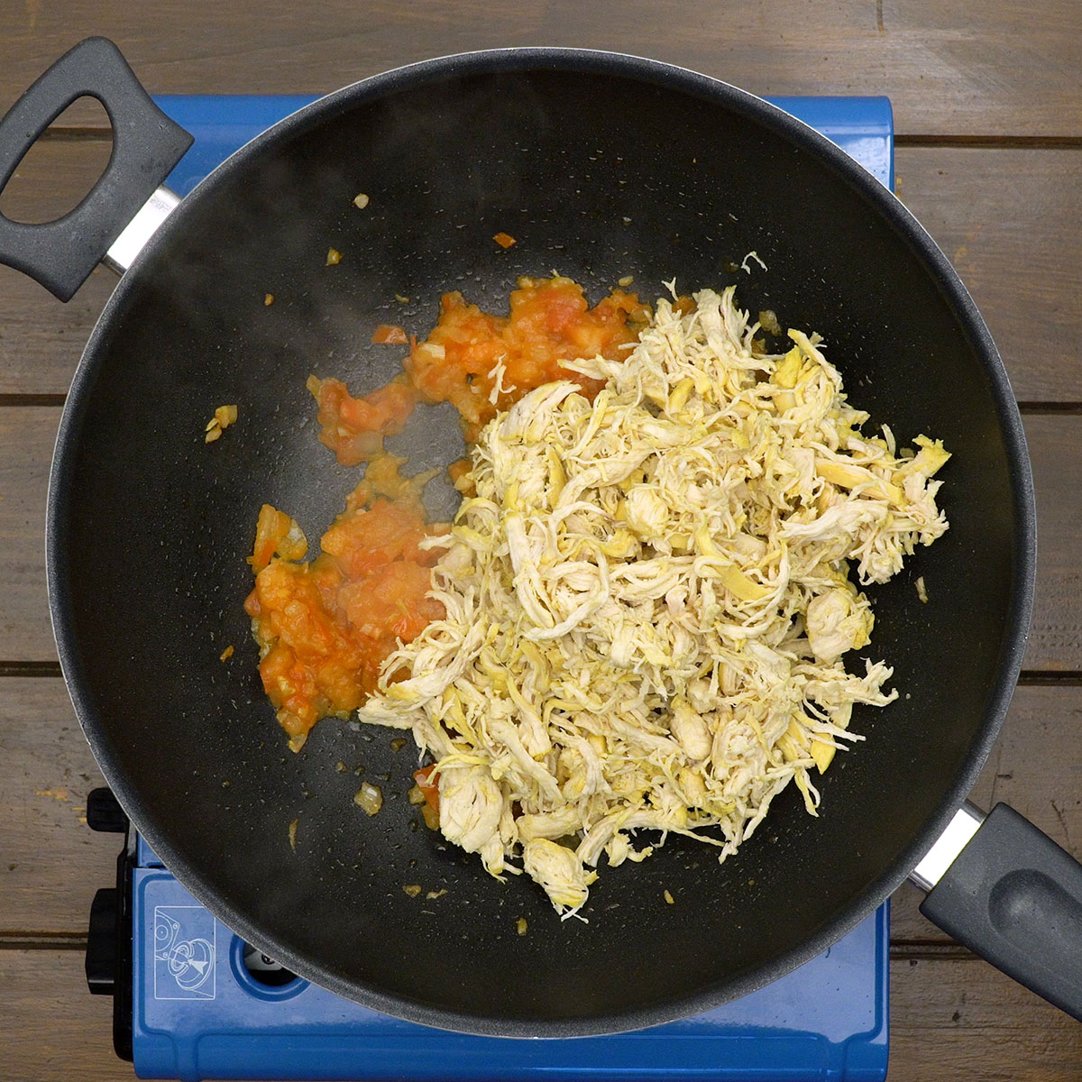 Shredded chicken sautéing with tomato and seasonings.