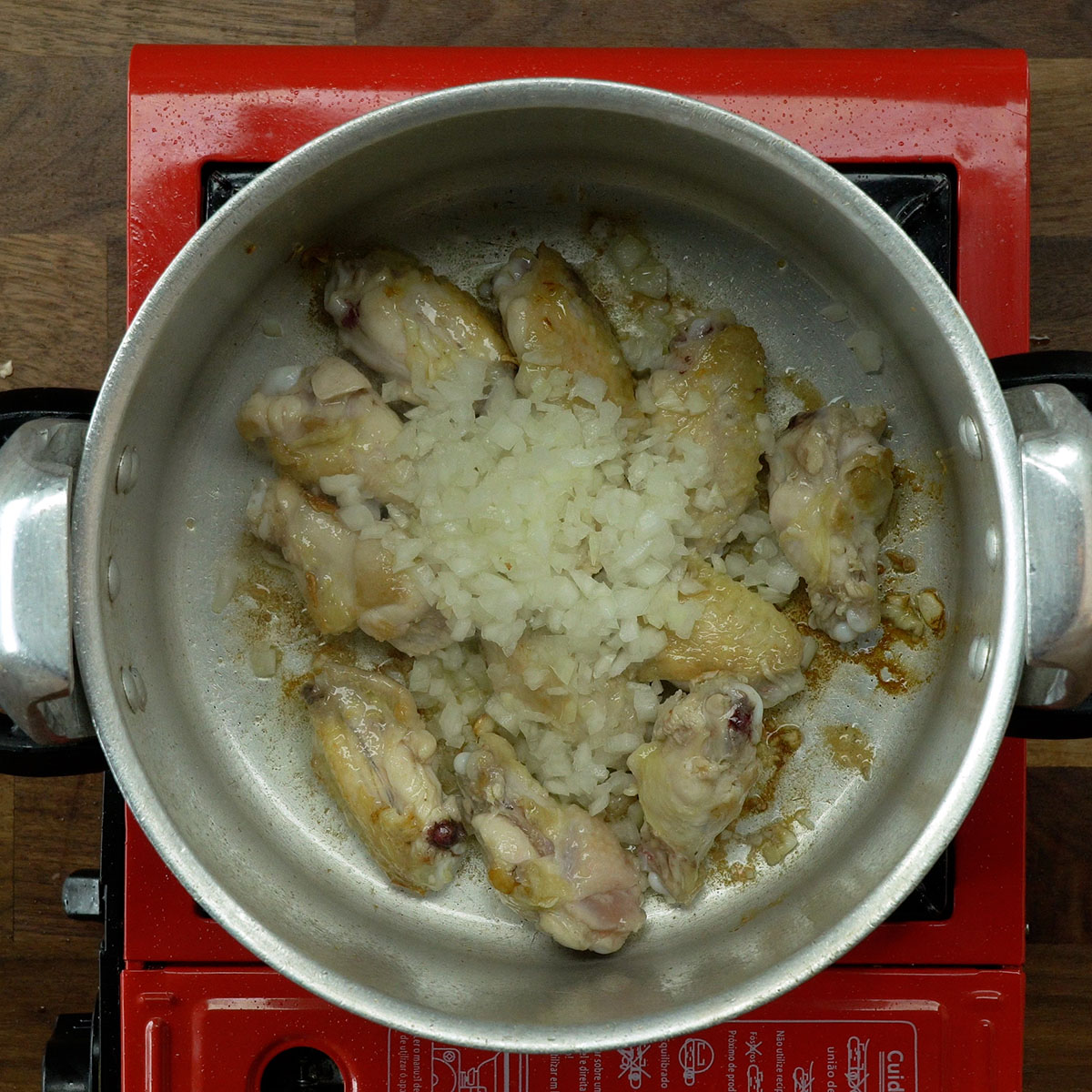 Chopped onion sautéing with browned chicken wings.