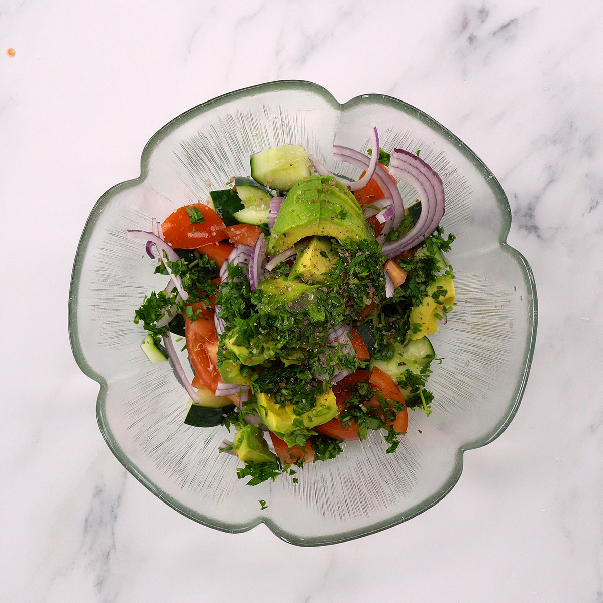 Avocado salad being seasoned with salt, pepper and fresh cilantro.