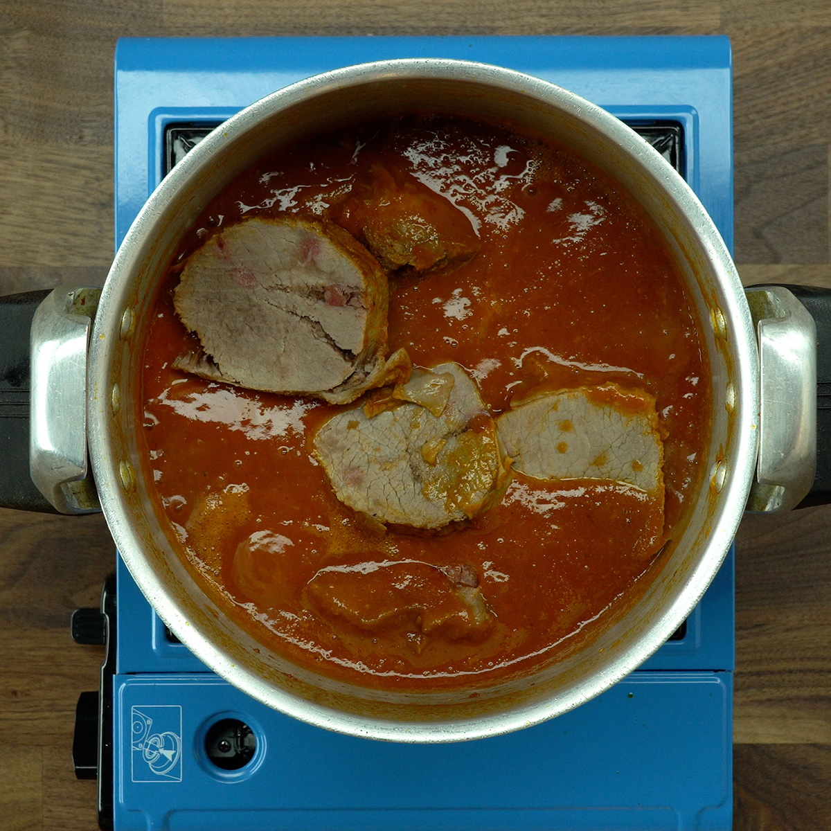 Sliced eye of round roast being mixed into the thick sauce in the pot.