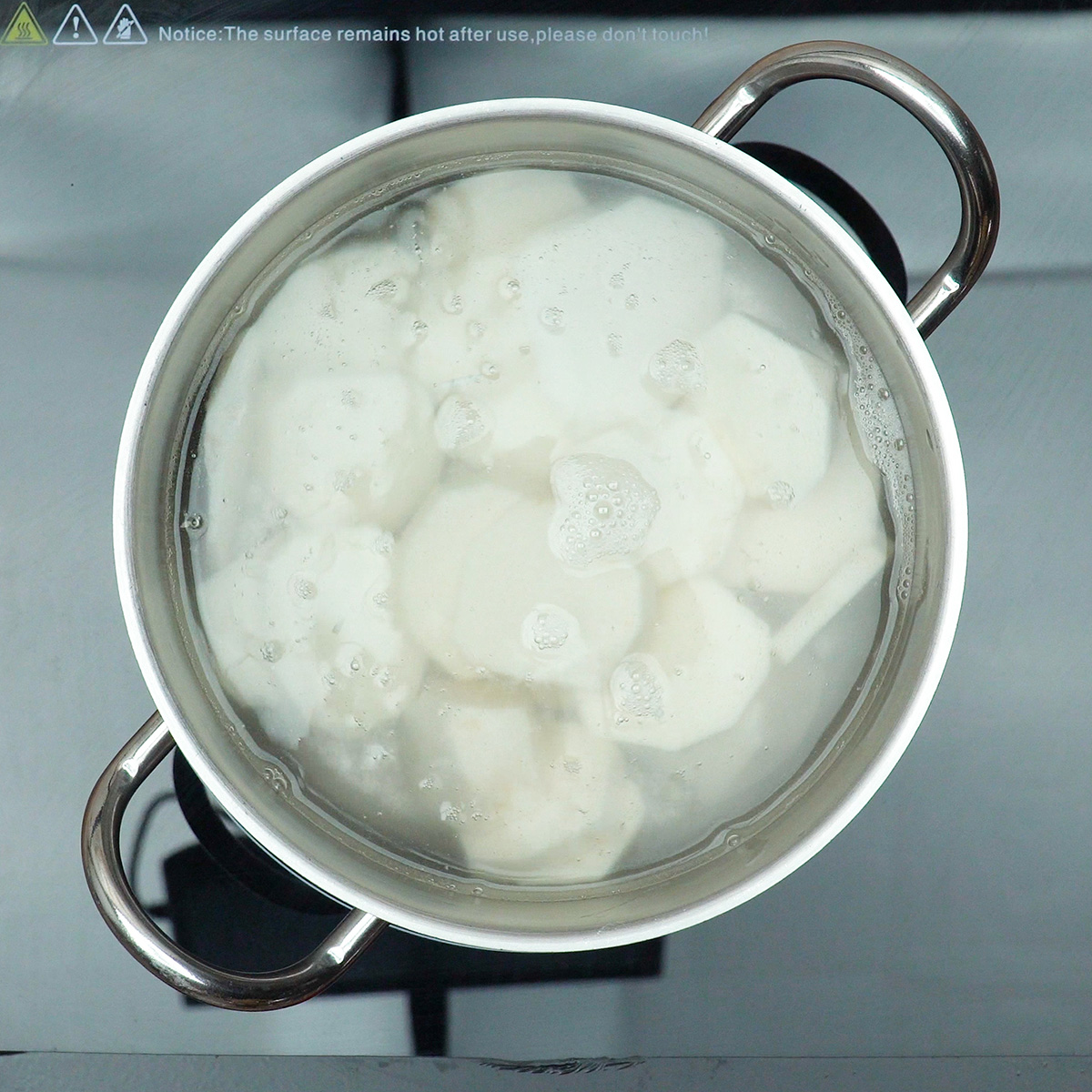 Pieces of white yam cooking in a saucepan with water until tender.