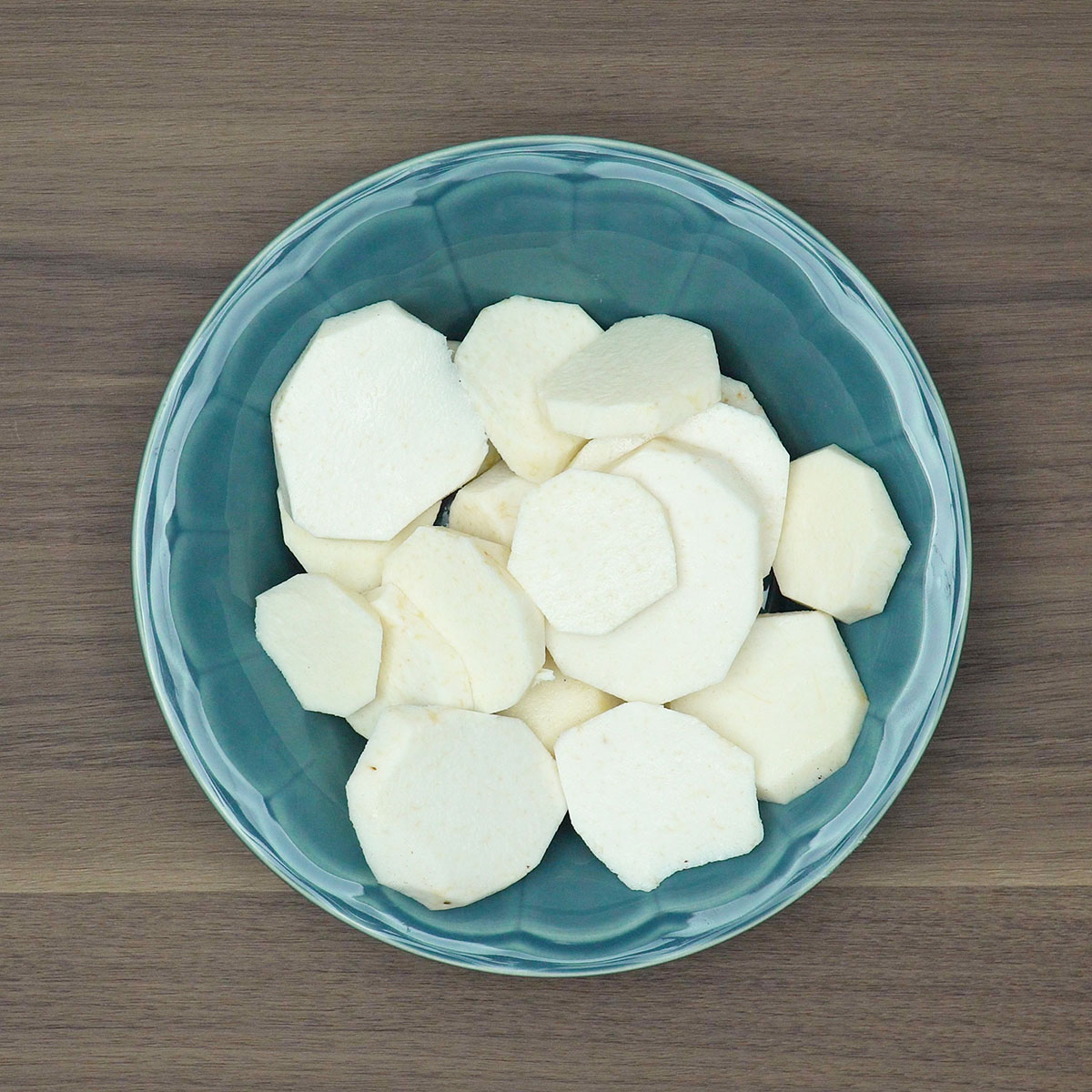 White yam being peeled and cut into medium pieces on a kitchen cutting board.