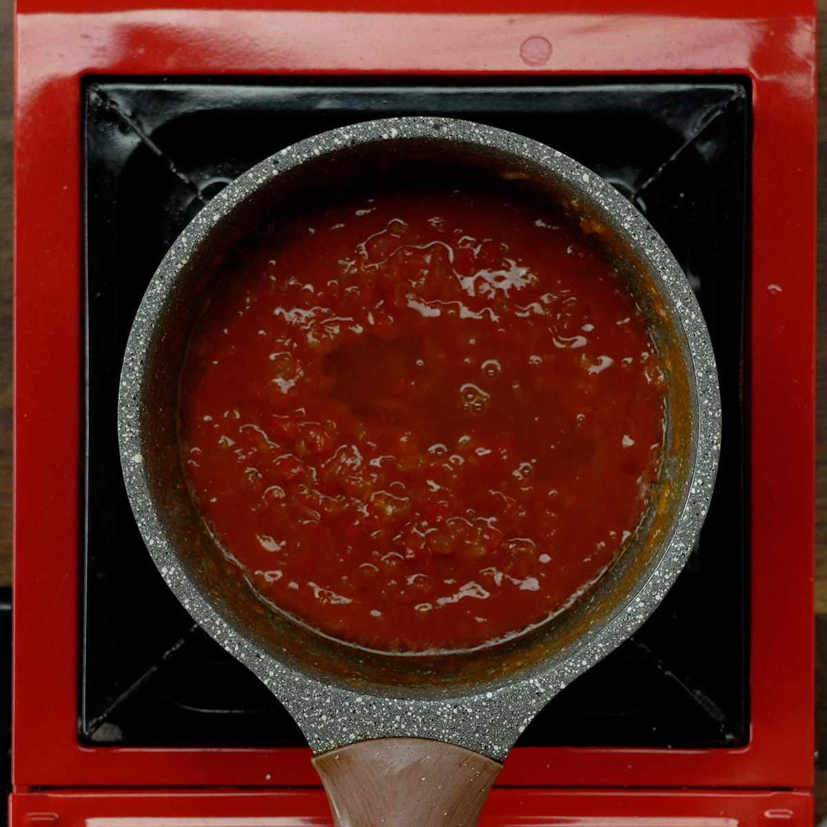 Tomato sauce cooking with sauteed vegetables in a skillet.